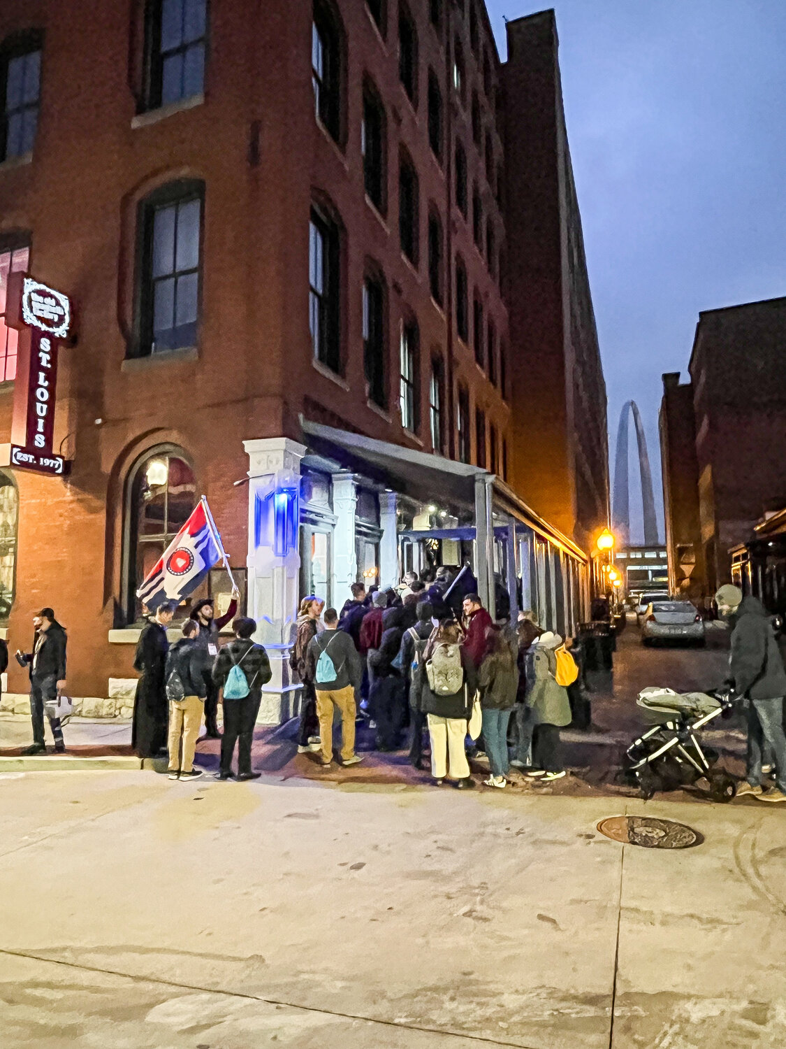 The end of the group arrives at a restaurant at Laclede’s Landing, with the Gateway Arch visible through the alley.